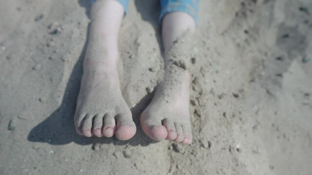 Teenage girl sitting on the beach throwing sand over her feet, closeup