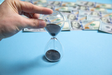 Male hand holding hourglass over dollars. Time is money