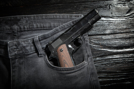 Pistol on jeans pocket on the dark background.