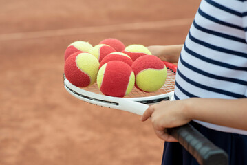 Kids player tennis. Racquet and legs and ball. Summer activities for children in the tennis club. Cropped image of sports little girl on tennis court. Athletic child girl hits tennis ball with a racke