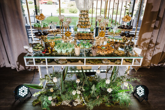Delicious wedding reception. Birthday candy bar on the background golden luxury decor. Celebration concept. Table with sweets, candies, dessert for party. Catering. Decorating an event in restaurant.