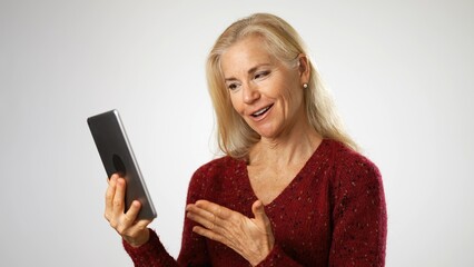 Fototapeta premium Elegant mature elderly woman wearing pearl necklace sitting on stool laughing clap hands, with copy space. Portrait of business woman emotions