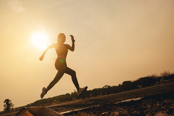 Silhouette of young woman running sprinting on road. Fit runner fitness runner during outdoor workout with sunset background.