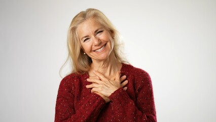 Mature woman, receives beautiful compliments, finally raises her hands puts hands on chest. Beautiful mature blond isolated on solid white background. Copy space