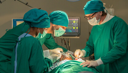 Team of surgery doctor in Operating Room, Assistant Hands out Instruments to Surgeons During Operation. doctor and nurse surgeons in green gown coat at hospital operating theater.