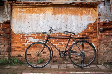Foto op Canvas Vintage bicycle on old rustic dirty wall house, many stain on wood wall. Classic bike old bicycle on decay brick wall retro style. Cement loft partition and window background. © BESTIMAGE