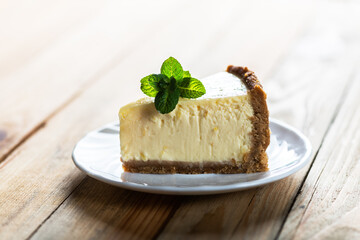 Piece of classic New York cheesecake with a sprig of mint on a plate on a wooden table. The concept of bakery and sweet cakes desserts