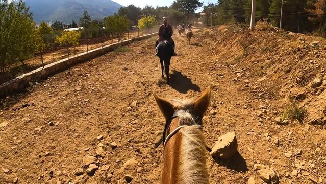 Group of people ride horses by mountain side trail in Turkey. POINT OF VIEW: Horseman's view from horse saddle while walking following behind women riding horses along path.High quality FullHD footage