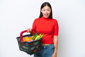 Plakat Young Asian woman holding a shopping basket full of food isolated on white background with surprise facial expression
