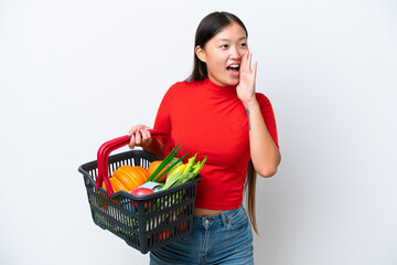 Obraz na płótnie Canvas Young Asian woman holding a shopping basket full of food isolated on white background shouting with mouth wide open to the side