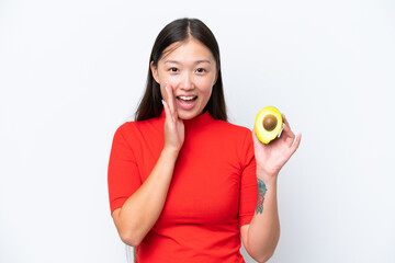 Young Asian woman holding an avocado isolated on white background shouting with mouth wide open