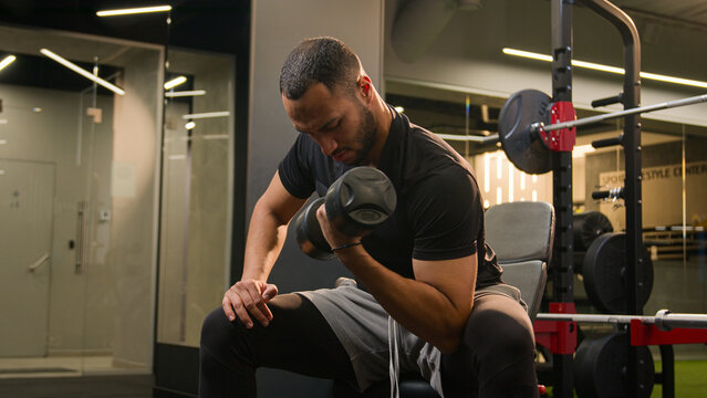 African American man in gym doing biceps workout exercise male sportsman strong power bodybuilder athlete in sport club hands arms training lifting up heavy dumbbell weights bicep curl fit burning fat
