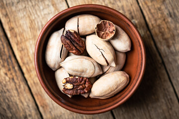 Dried organic Pecan nuts in orange ceramic bowl on wooden table closeup. Food photography