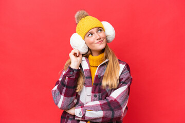 Young beautiful woman wearing winter muffs isolated on red background thinking an idea