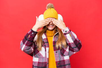 Young beautiful woman wearing winter muffs isolated on red background covering eyes by hands