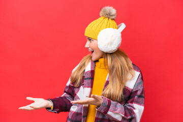 Young beautiful woman wearing winter muffs isolated on red background with surprise facial expression
