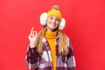 Young beautiful woman wearing winter muffs isolated on red background saluting with hand with happy expression