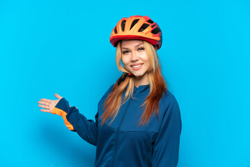 Young cyclist girl isolated on blue background extending hands to the side for inviting to come