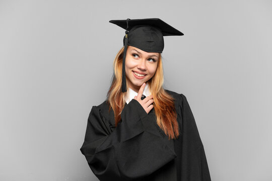Young university graduate girl over isolated background looking up while smiling