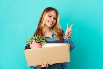 Naklejka premium Teenager blonde girl making a move while picking up a box full of things smiling and showing victory sign