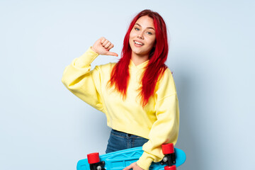 Teenager red hair girl isolated on blue background with a skate with happy expression