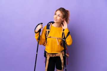 Teenager girl with backpack and trekking poles over isolated purple background thinking an idea