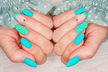 Turquoise nail art female manicure on a light wooden background. Long almond-shaped nails. Close-up of a woman's hands with a delicate manicure on her nails