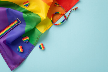 LGBT History Month theme. Flat lay top view of symbolic parade items, including rainbow flag, wristlet, pin badges, colorful hearts, on pastel blue surface with a blank space for text