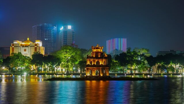 HANOI, VIETNAM - MAY, 2023: Night timelapse of old Hoan Kiem Lake, Traffic flow, cars and motobikes passing with light trails by night.