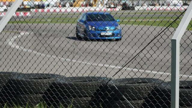 Racing track fencing made of metal mesh and car tires. Blue sports hatchback turns bunch during free practice sessions on race day under sunlight.