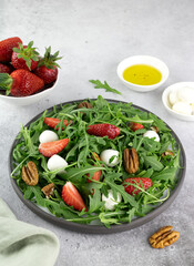 Salad with strawberries, mozzarella balls, arugula and pecans on gray background