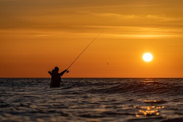 Silhouette eines Angler in wasserdichten Hosen welcher  vor einem traumhaften orangen...
