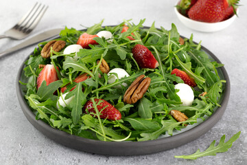 Salad with strawberries, mozzarella balls, arugula and pecans on gray background