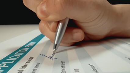 Closeup macro shot movement of applicant's hand filling personal information and writing name on job application form document. Employment and job opportunity for unemployed candidate.