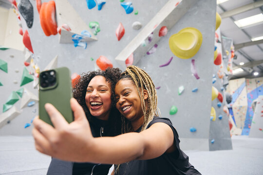 Two Smiling Female Friends Posing For Selfie By Climbing Wall At Indoor Activity Centre