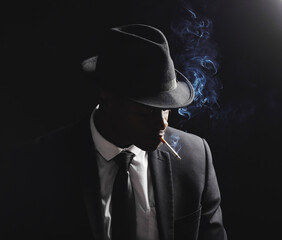 Man, gangster and cigarette in studio by black background with smoke, silhouette and dangerous in shadow. Mafia, secret agent or male in night for smoking with vintage aesthetic by dark backdrop