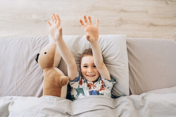 Cute little happy child boy playing, having fun at home. Healthy child, sweetest toddler boy sleeping in a bed with his lovely toy. Time before a sleeping. Happy morning time
