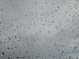 Background of rain drops on glass with blue sky and white clouds.