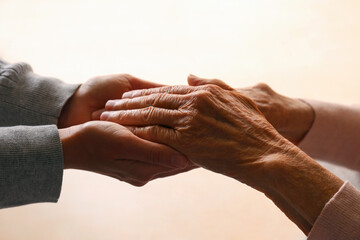 Fototapeta premium Cropped studio shot of elderly woman and female geriatric social worker holding hands. Women of different age comforting each other. Close up, background, copy space.