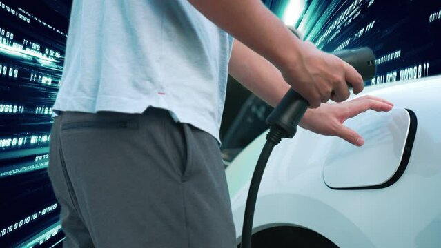Progressive man charge electric car with power cable plug from charging station with technology background of binary code flying through votex. EV car concept with modern technology.