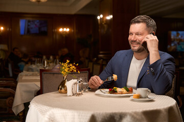 Handsome man eating at lobby-bar and talking smartphone