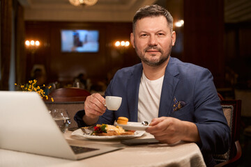 Fototapeta na wymiar Man enjoying coffee and breakfast in lobby bar with free wi-fi