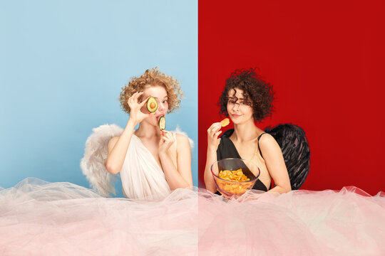 Make your choice. Girl in image of angel eating avocado and woman, devil, eating chips against blue red background. Concept of healthy and unhealthy eating, beauty, comparison of being, creativity