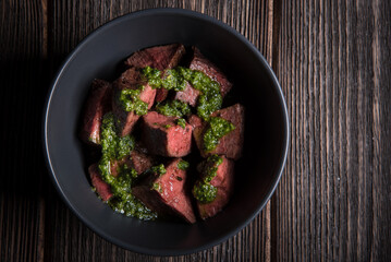 Fried slices of beef tenderloin in pesto sauce in a deep plate on a wooden table.