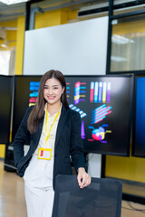 Fototapeta premium Successful businesswoman standing in creative office and looking at camera. Woman entrepreneur in a coworking space smiling. Portrait of beautiful business woman standing