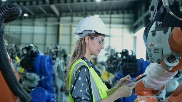 A female engineer installs a program on a robotics arm in a robot warehouse. And test the operation before sending the machine to the customer.
