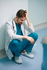 Upset young doctor squatting in the hospital corridor
