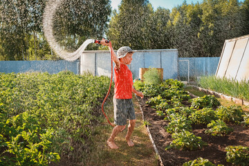 boy child jumping splashing hose water in the backyard in the garden in summer at sunset in the...