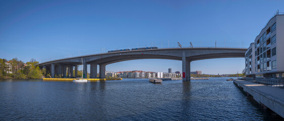 The bay at the Essinge islands in the sea Mälaren, tram passing on a high bridge and waterfront modern apartment houses, a sailing boat passing  to the archipelago, an sunny early summer day in Stockh