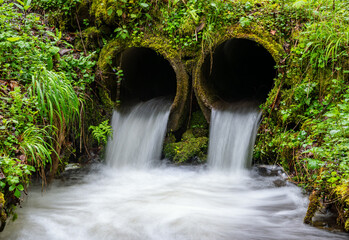Water of a small creek in Iserlohn Sauerland Germany flowing out of two parallel concrete tubes...
